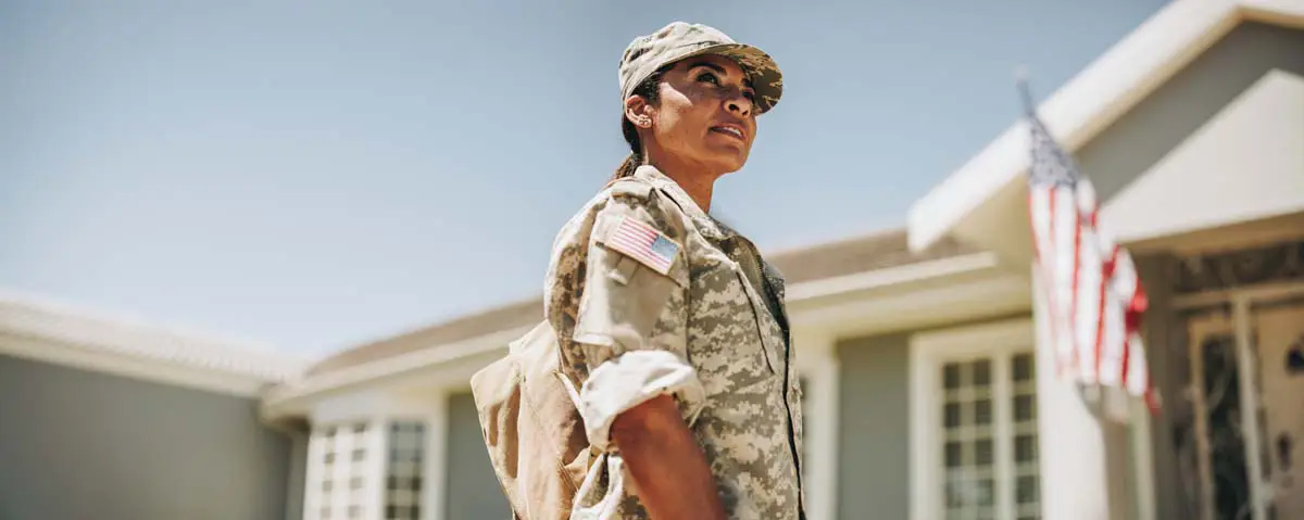 Service member standing in front of a suburban home with an American flag